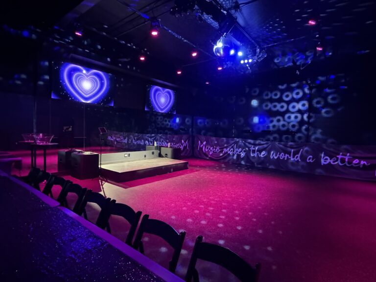 Event space with purple heart screens, sparkly table, and "Music makes the world a better place" banner.