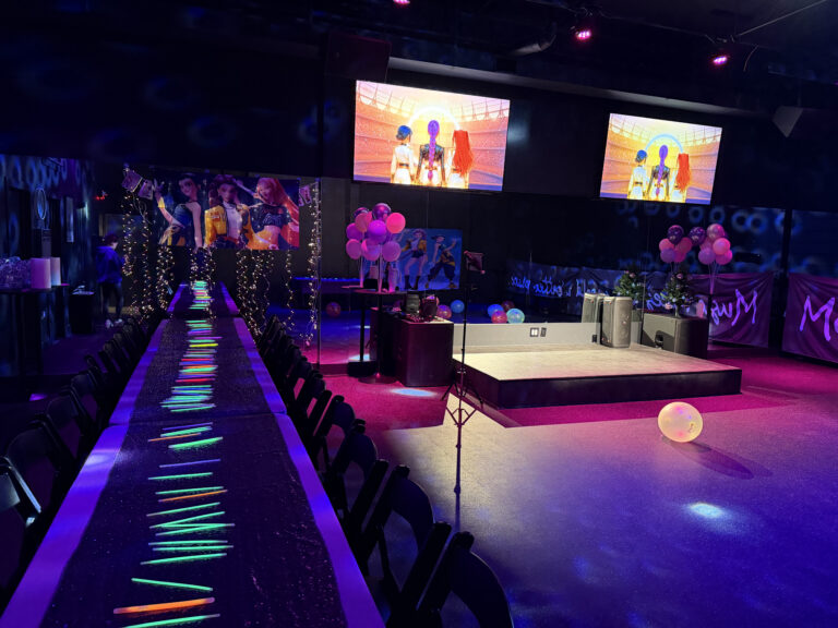 Vibrant party venue with colorful decorations, glowing table, and screens displaying animated characters for a festive atmosphere.