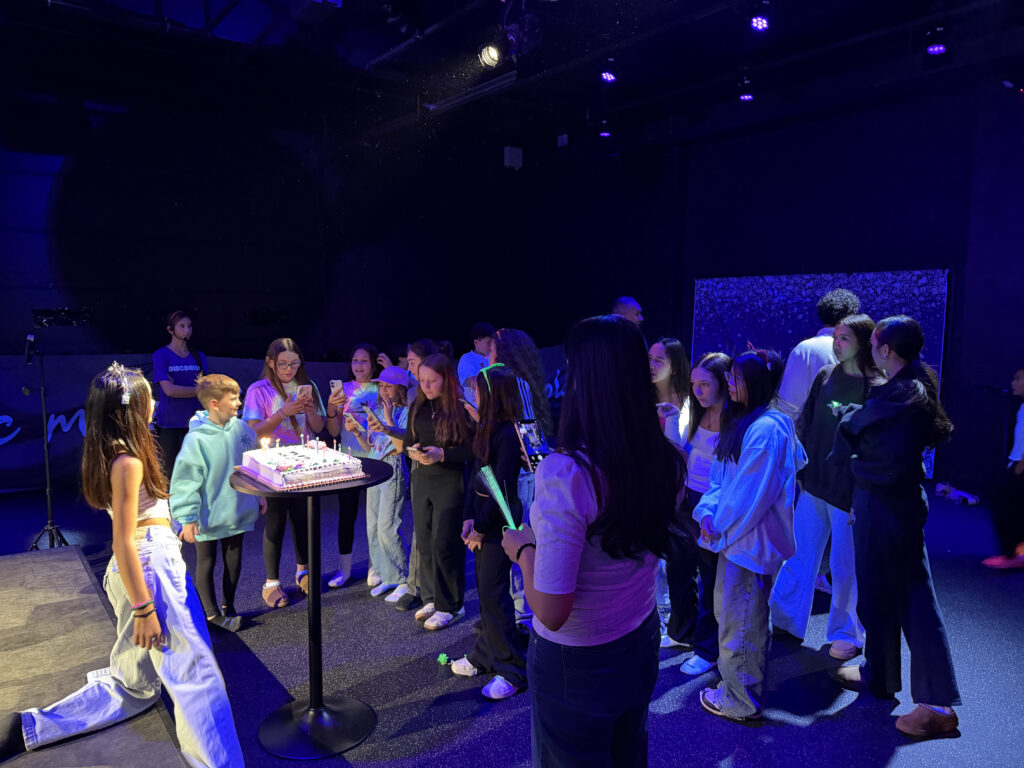 A group of children celebrating a birthday with a cake, enjoying the party atmosphere in a vibrant indoor setting.
